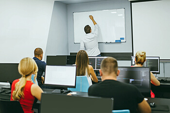 Praesenzstudium Studenten im Seminar vor PC´s und Dozent an der Tafel