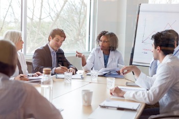 Gesundheitsmanager/innen und Ärzt/innen sitzen an Besprechungstisch und diskutieren