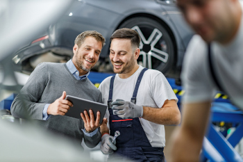 Dienstleistungsmanager erklärt einem Kfz-Mechaniker etwas auf seinem Tablet